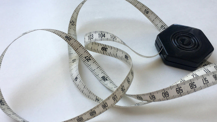 A small black tape measure is open and tangled against a white background.