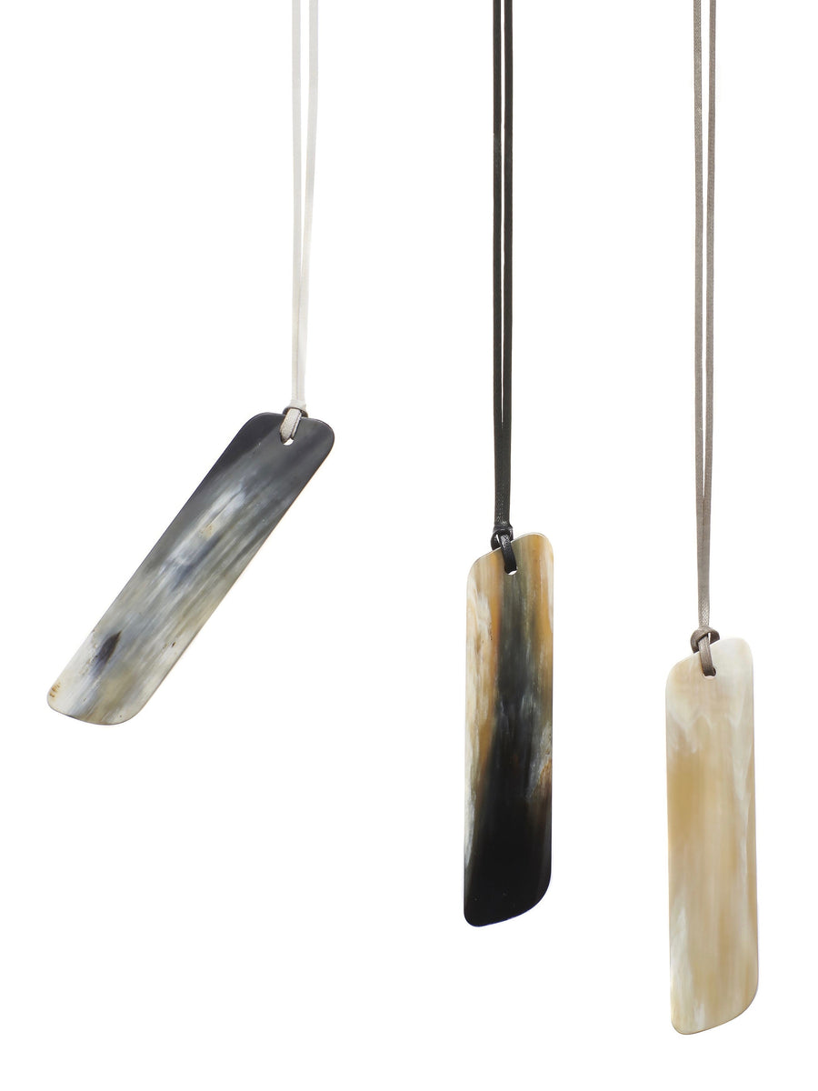 A pendant necklace made from black, white, and gold natural horn in a rectangular shape, hung from an adjustable coated cotton cord.