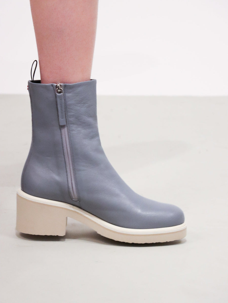 Slate blue demi boot with a heeled taupe foam sole, topped with a layer of rubber, and off-white welting.